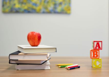 books on desk with apple, ABC blocks and colored pencils